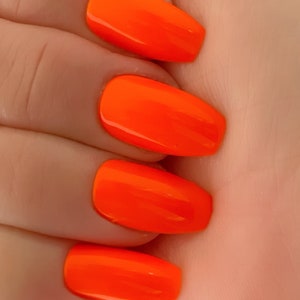 May include: Close-up of four fingernails painted with bright orange nail polish. The nails are long and oval-shaped.