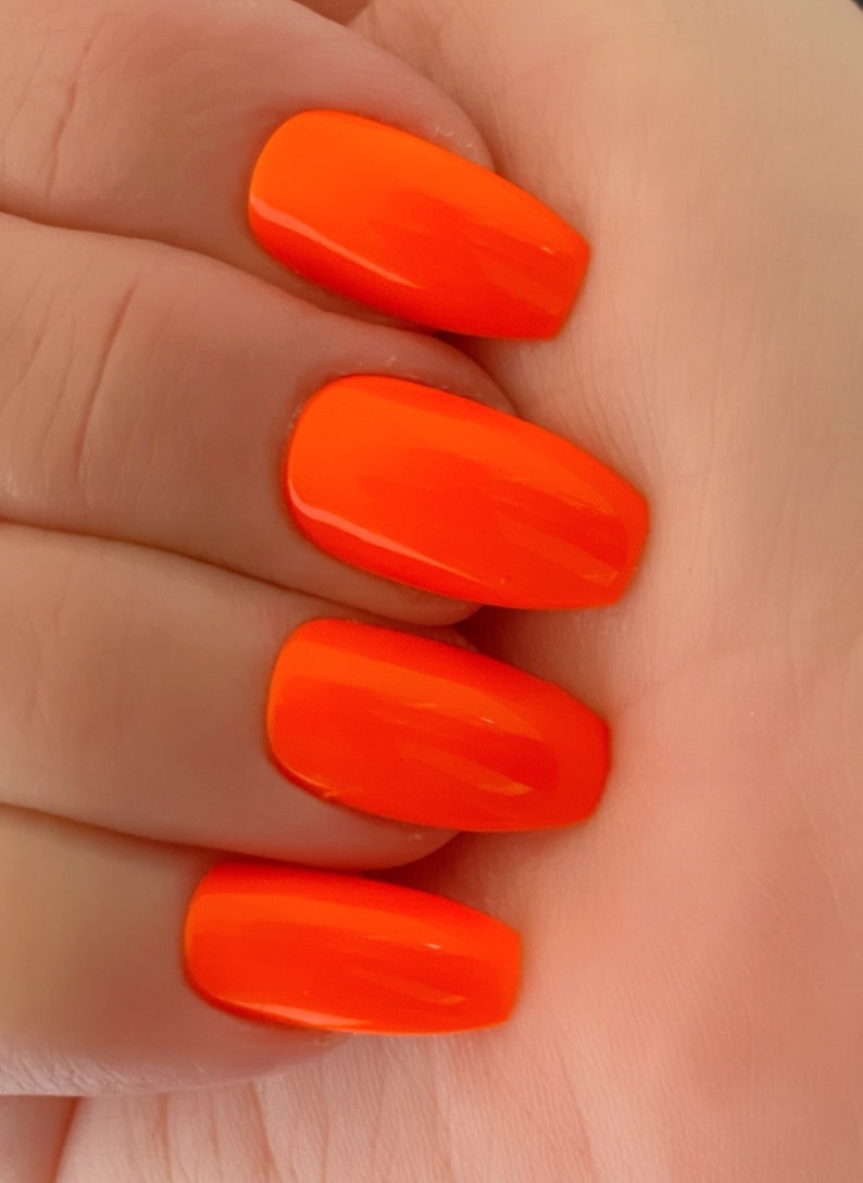 May include: Close-up of four fingernails painted with bright orange nail polish. The nails are long and oval-shaped.