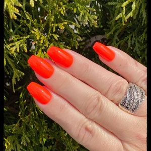 May include: A hand with bright orange nail polish on each finger. The hand is wearing a silver ring with black stones.