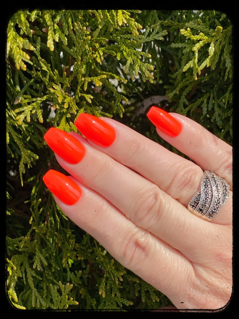 May include: A hand with bright orange nail polish on each finger. The hand is wearing a silver ring with black stones.