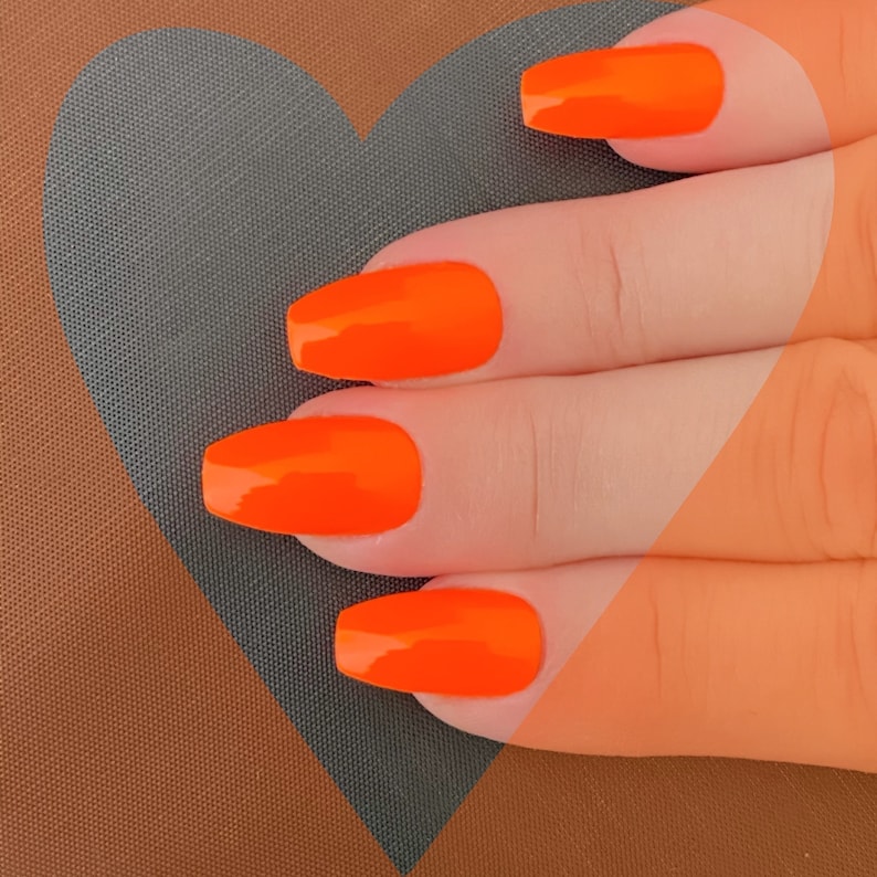 May include: Close-up of a hand with four long, orange-painted nails. The nails are shaped into a coffin shape and have a glossy finish.