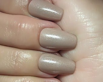 May include: Close-up of four fingernails with a light brown shimmer nail polish.