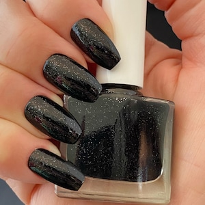 May include: Black nail polish with a glittery finish. The bottle is clear and has a white cap.