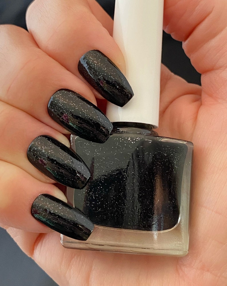 May include: Black nail polish with a glittery finish. The bottle is clear and has a white cap.