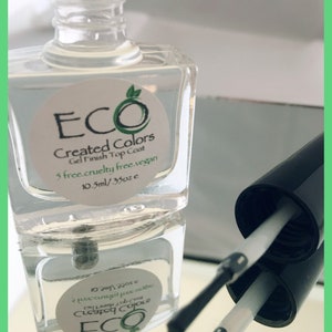 May include: A clear glass bottle of ECO Created Colors Gel Finish Top Coat. The bottle is labeled with the brand name, product name, and size: 10.5ml/.35oz. The bottle is sitting on a reflective surface.