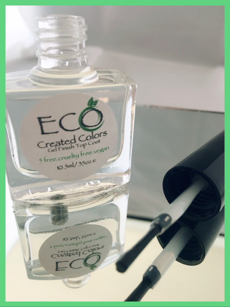 May include: A clear glass bottle of ECO Created Colors Gel Finish Top Coat. The bottle is labeled with the brand name, product name, and size: 10.5ml/.35oz. The bottle is sitting on a reflective surface.