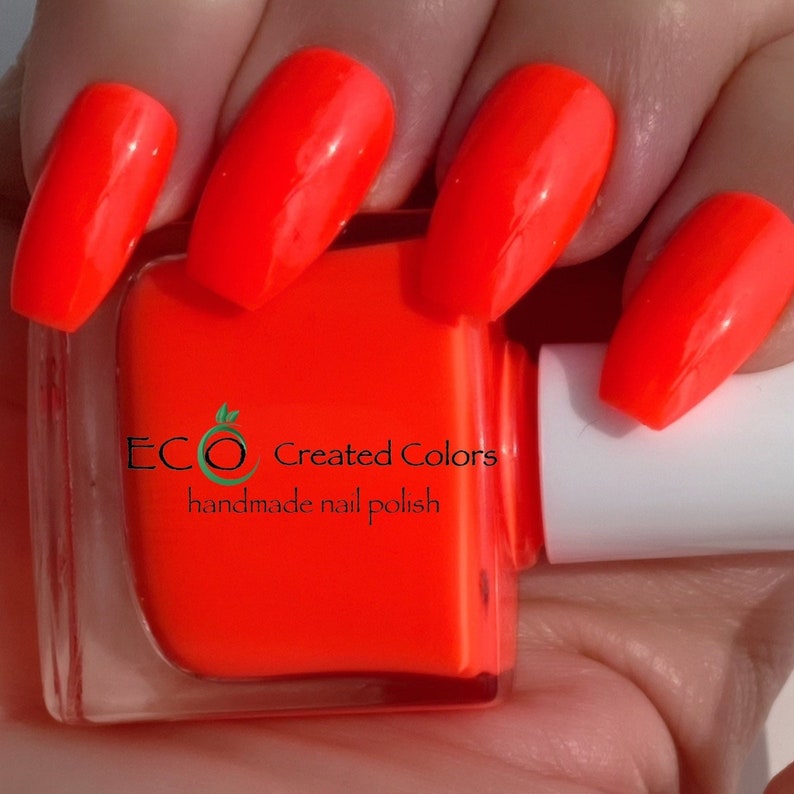 May include: A bottle of bright orange nail polish with the text "ECO Created Colors handmade nail polish" on the label. A hand is shown with several nails painted in the same bright orange color.