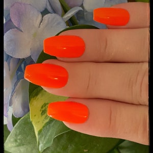 May include: Close-up of a hand with four bright orange nail polish tips. The nails are long and square shaped.