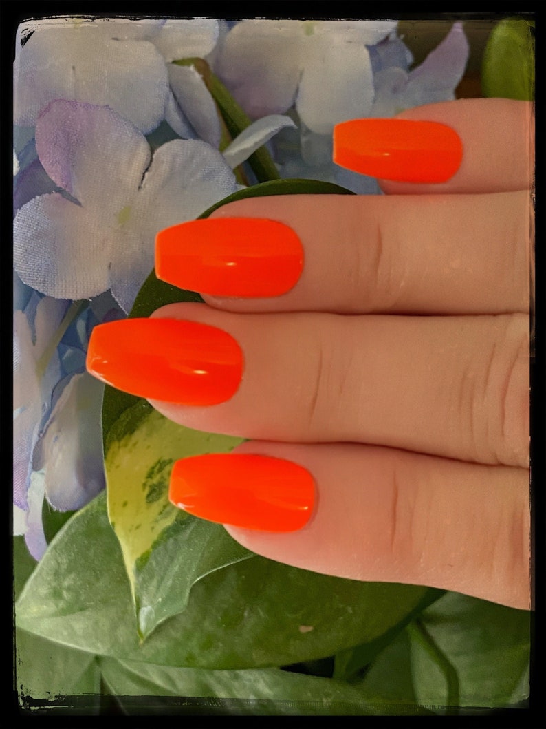 May include: Close-up of a hand with four bright orange nail polish tips. The nails are long and square shaped.