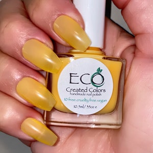 May include: A yellow nail polish bottle with a white label that reads "ECO Created Colors handmade nail polish 10 free.cruelty free.vegan 10.5ml/.35oz e"