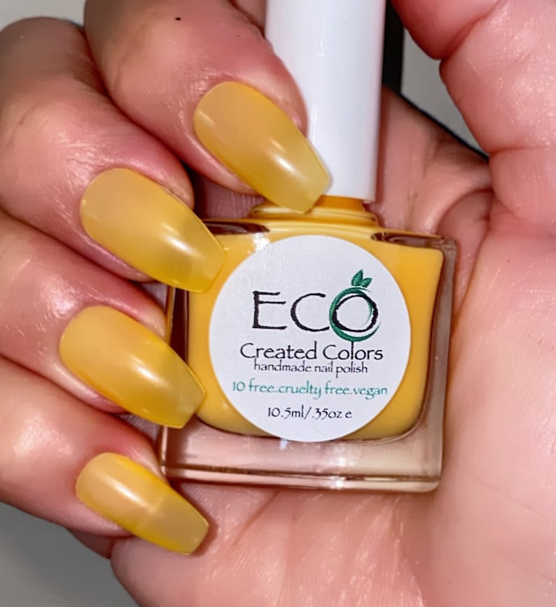 May include: A yellow nail polish bottle with a white label that reads "ECO Created Colors handmade nail polish 10 free.cruelty free.vegan 10.5ml/.35oz e"