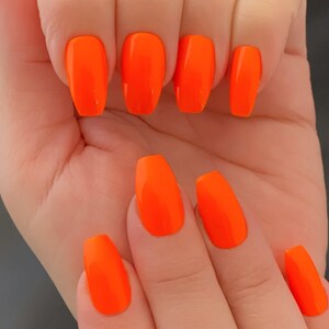 May include: Close-up of hands with bright orange nail polish on long, oval-shaped nails.
