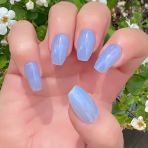 May include: A hand model wearing light blue, long, almond-shaped press-on nails with a marbled design.