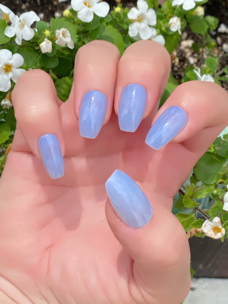 May include: A hand model wearing light blue, long, almond-shaped press-on nails with a marbled design.
