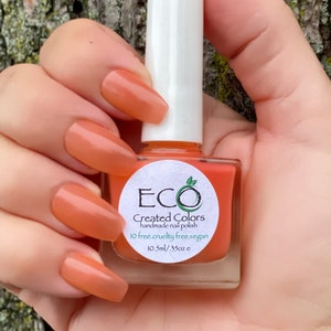 May include: A bottle of orange nail polish with a white label that reads "ECO Created Colors handmade nail polish 10 free.cruelty free.vegan 10.5ml/.35oz e"
