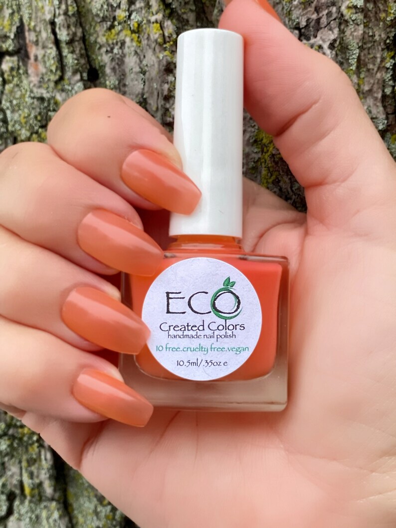 May include: A bottle of orange nail polish with a white label that reads "ECO Created Colors handmade nail polish 10 free.cruelty free.vegan 10.5ml/.35oz e"
