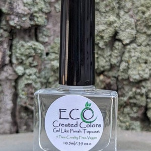 May include: A clear glass bottle of ECO Created Colors Gel Like Finish Topcoat nail polish. The bottle is 10.5 ml or 0.35 oz and is labeled as cruelty-free and vegan.