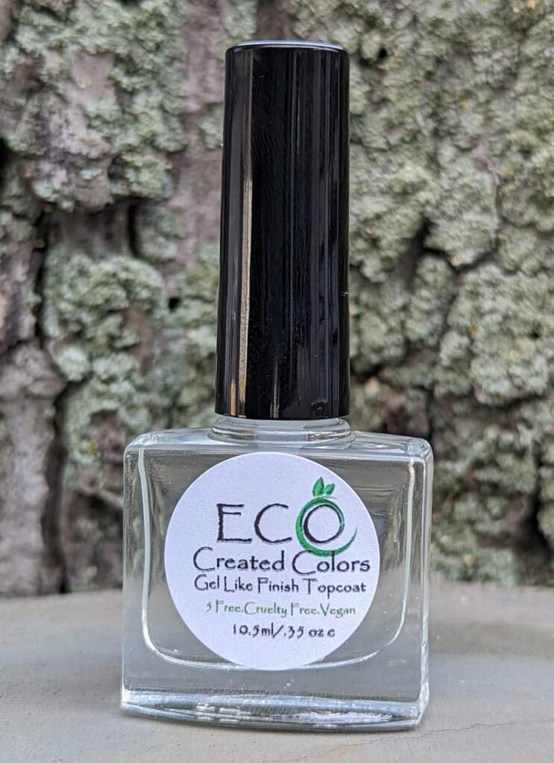 May include: A clear glass bottle of ECO Created Colors Gel Like Finish Topcoat nail polish. The bottle is 10.5 ml or 0.35 oz and is labeled as cruelty-free and vegan.