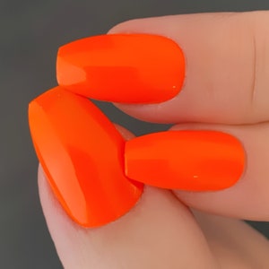 May include: Close-up of two fingernails painted with bright orange nail polish. The nails are oval shaped and the polish is glossy.