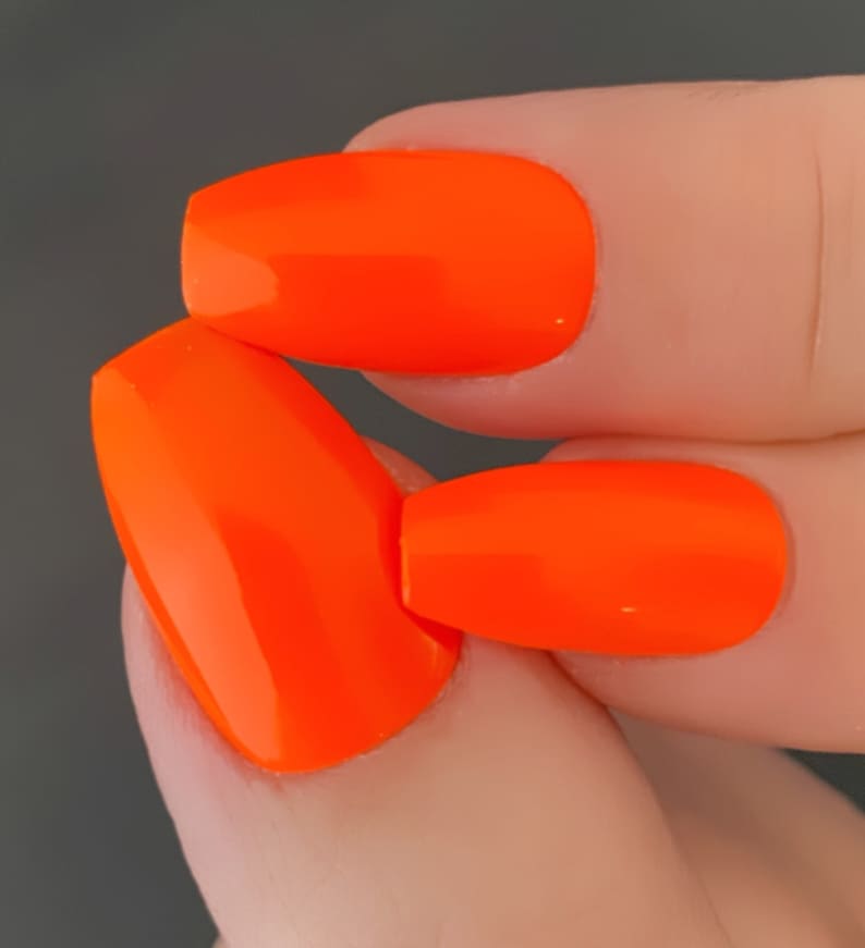 May include: Close-up of two fingernails painted with bright orange nail polish. The nails are oval shaped and the polish is glossy.