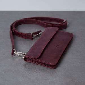 May include: A rectangular burgundy leather crossbody bag with a fold-over flap, a matching adjustable shoulder strap, and silver-toned metal hardware clips. The word "MORTE" is embossed in small capital letters on the front flap of the bag.