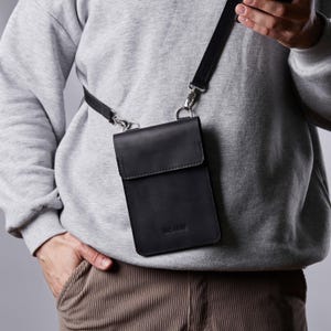 May include: A black leather crossbody bag with a silver strap and a silver buckle. The bag has a flap closure and a small pocket on the front. The bag is labeled "remarkable".