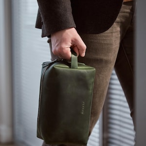 May include: A dark green leather travel wash bag with a zip closure and a top handle. The bag has the word "Sincerely" embossed on the front.