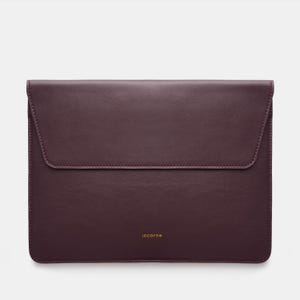 May include: A dark plum-colored rectangular laptop sleeve with a smooth finish and a flap closure. The word "incarne" is printed in small gold letters near the bottom center of the front panel. The sleeve features clean, tonal stitching along the edges.