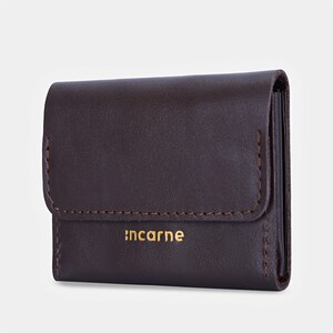 May include: A dark brown leather wallet featuring a fold-over flap with visible stitching along the edges. The word "incarne" is embossed in gold lettering on the front surface of the wallet, which has a smooth, matte finish and a compact design.
