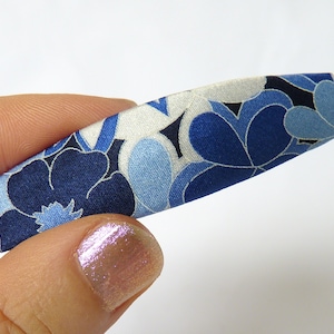 May include: A blue and white floral patterned hair clip. The clip is made of fabric and has a curved shape.