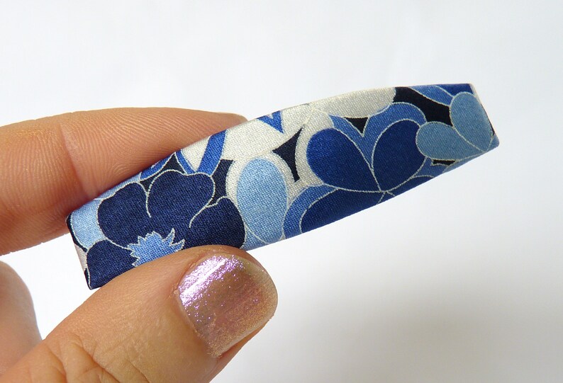 May include: A blue and white floral patterned hair clip. The clip is made of fabric and has a curved shape.