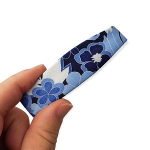 May include: A blue and white floral patterned fabric hair clip. The clip is about 5 inches long and has a slightly curved shape.