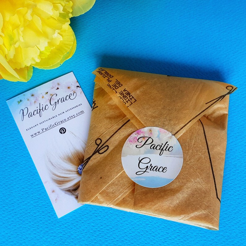 May include: A brown paper package with a white circle sticker that says "Pacific Grace" in cursive. The package is sitting on a blue surface. The sticker has a watercolor floral design.