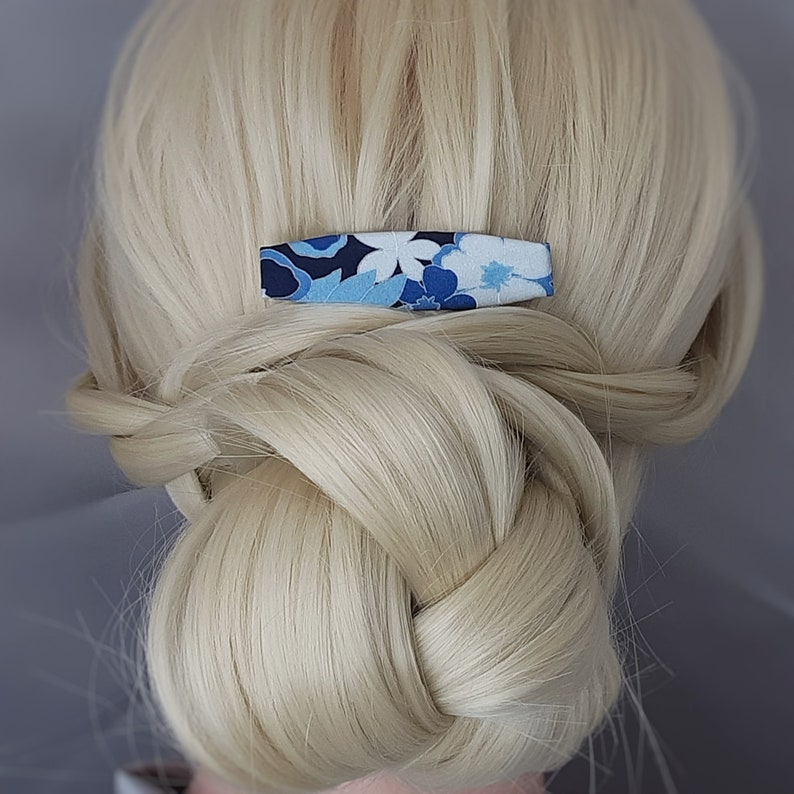 May include: A blue and white floral patterned hair clip. The clip is made of fabric and has a simple design.