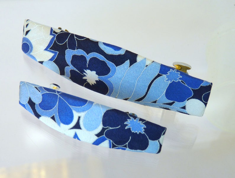 May include: Two blue and white floral patterned hair clips with gold metal clasps.