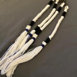 Peut inclure: Quatre pompons en corde blanche avec des accents noirs et bleus. Chaque pompon est attaché à un fermoir en métal. Les pompons sont posés sur une surface grise. Les pompons sont faits d'une matière douce et tissée.