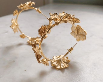 May include: Gold hoop earrings with a floral design. The earrings are made of metal and have a delicate, intricate design.