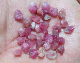 May include: A collection of small, pink ruby gemstones. The rubies are rough and have a variety of shapes and sizes.