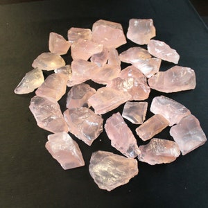Puede incluir: Una colección de cristales de cuarzo rosa, algunos con una apariencia translúcida, dispuestos sobre una superficie negra.