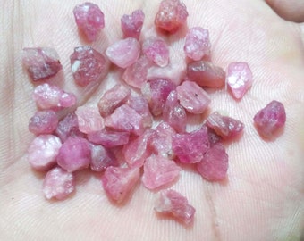 May include: A handful of raw, uncut pink gemstones. The stones vary in size and shape, with a range of pink hues from light to deep rose. The rough texture and natural forms suggest these are unpolished crystals, perfect for jewelry making or collecting.