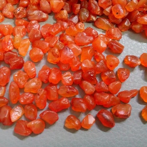 K&ouml;nnte beinhalten: Eine Sammlung kleiner, glatter, orangefarbener Karneol-Steine. Die Steine sind unregelm&auml;&szlig;ig geformt und haben eine nat&uuml;rliche, polierte Oberfl&auml;che.
