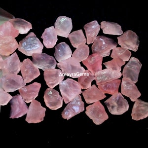 Pode incluir: Uma coleção de pedras brutas de quartzo rosa. As pedras são de vários tamanhos e formas, com uma cor rosa claro translúcida.