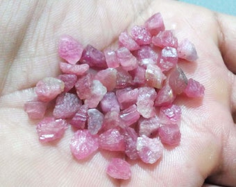 May include: A pile of pink and white rough ruby gemstones. The gemstones are small and have a variety of shapes and sizes.