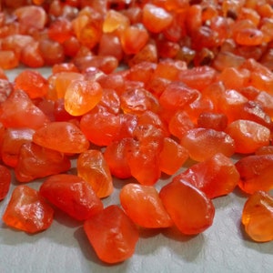 K&ouml;nnte beinhalten: Nahaufnahme eines Haufens Karneol-Edelsteine. Die Steine sind tief orange-rot und haben eine glatte, polierte Oberfl&auml;che.