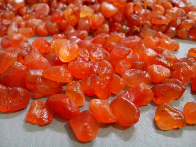 K&ouml;nnte beinhalten: Nahaufnahme eines Haufens Karneol-Edelsteine. Die Steine sind tief orange-rot und haben eine glatte, polierte Oberfl&auml;che.