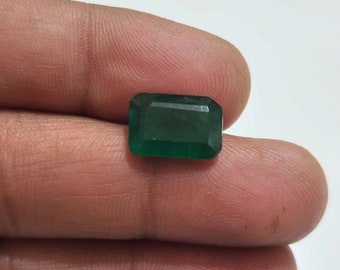 May include: A deep green emerald gemstone cut in a rectangular shape.