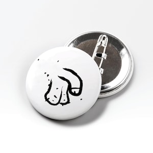 May include: Two white round buttons. The front button has a black illustration of a hand pointing down. The second button is behind the first, showing the pin back. The buttons are on a white background.