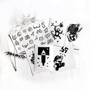May include: A collection of black and white stickers with various designs, including a monkey, shark, and Mario. Some stickers feature text like "LOVE LIFE" and "COOL". The stickers are arranged on a white surface.