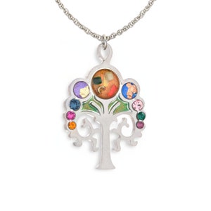 May include: A silver tree of life pendant necklace with colorful gemstones. The pendant features a green tree with a silver trunk and branches. The tree is surrounded by seven colorful gemstones, including purple, blue, green, orange, red, and pink.