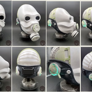 May include: A white helmet with a black strap and green accents. The helmet has a gas mask attached to it. The helmet is on a stand.